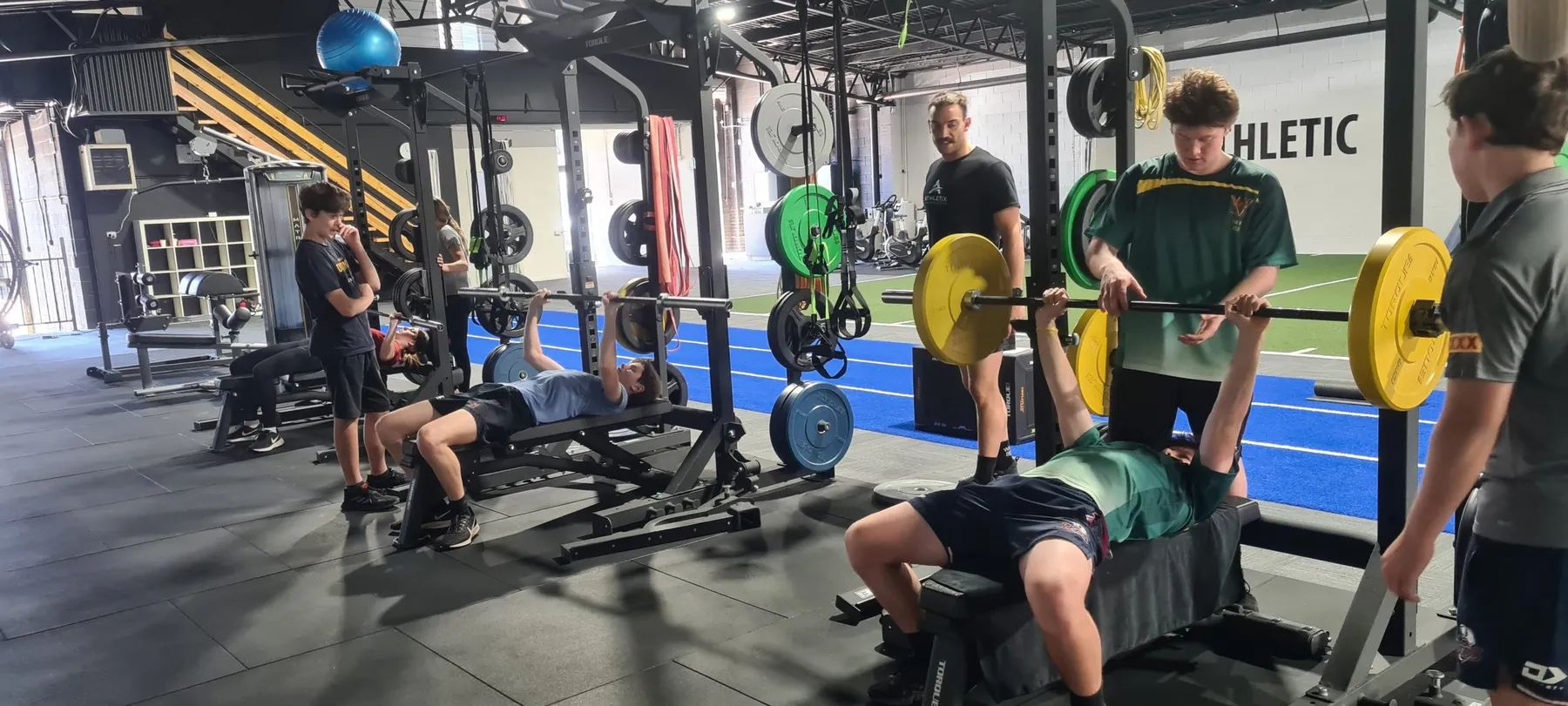Teen athletes bench pressing under coach supervision at ATHLETIX Brisbane